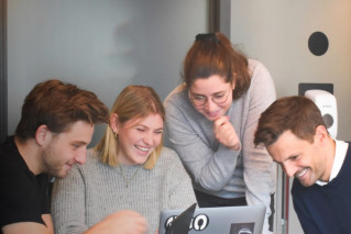 Vier fröhliche junge Menschen arbeiten gemeinsam an einem Laptop.