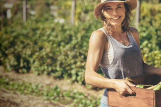 Eine Frau trägt eine Kiste frisch geerntetes Gemüse vom Feld.