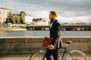 Nachhaltigkeit - Ein Mann in einem Anzug schiebt sein Fahrrad über eine Brücke.