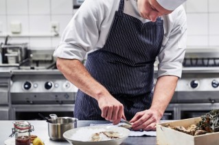 A young chef is arranging food on a plate.