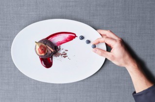 Close-up on a hand that is artfully arranging food on a plate.