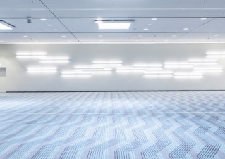 A room with light-blue carpet, white walls, bright LED lights and a low ceiling.