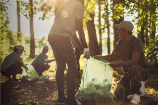 A group of people in a sunny forest. They are collecting garbage in big bags.